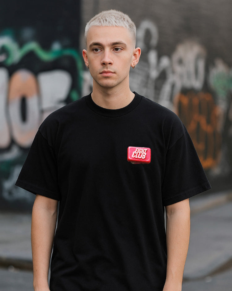 Person wearing a black t-shirt with a red logo in front of graffiti art.